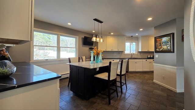 kitchen featuring plenty of natural light, white cabinets, a kitchen island, decorative light fixtures, and a baseboard radiator