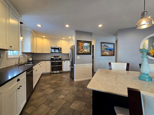 kitchen with sink, appliances with stainless steel finishes, white cabinetry, hanging light fixtures, and decorative backsplash