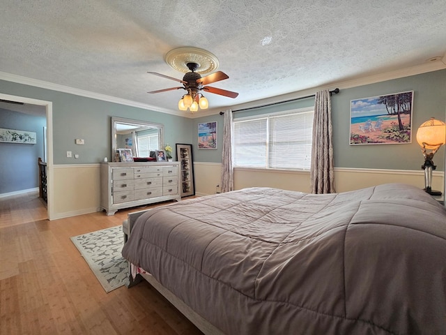 bedroom featuring ceiling fan, ornamental molding, light hardwood / wood-style flooring, and a textured ceiling