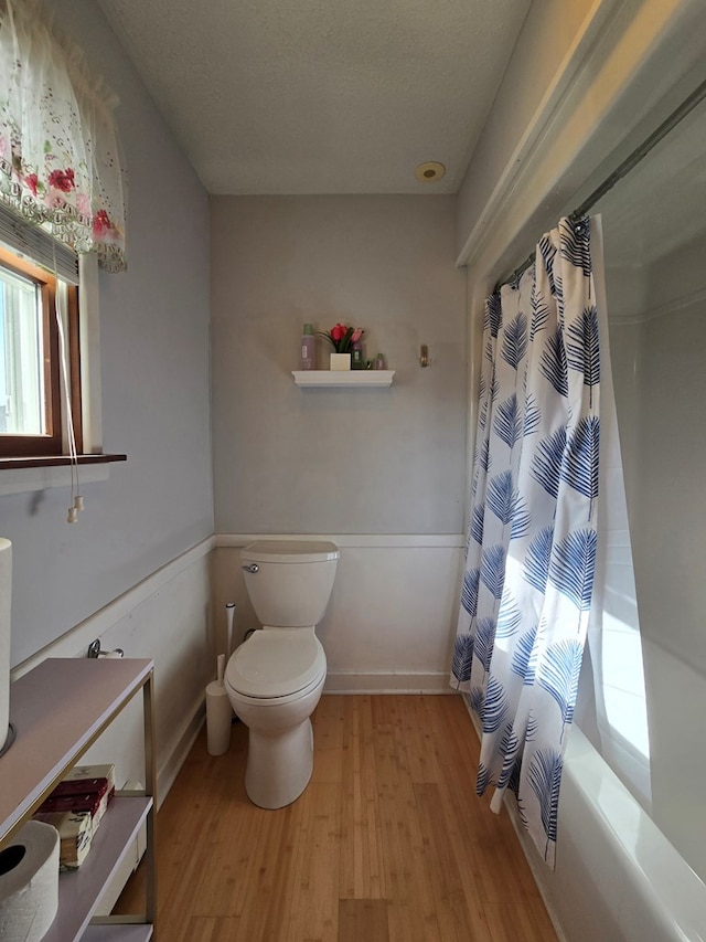 bathroom with wood-type flooring, a textured ceiling, shower / bath combo with shower curtain, and toilet