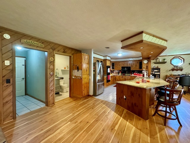 kitchen with light hardwood / wood-style flooring, a center island, stainless steel refrigerator with ice dispenser, light stone countertops, and a textured ceiling