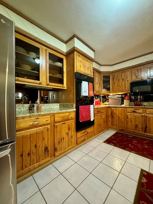 kitchen featuring light stone counters, light tile patterned floors, black appliances, and a textured ceiling