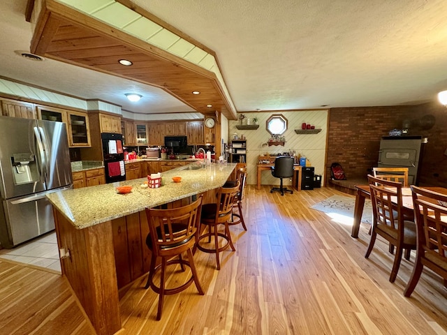 kitchen with a wood stove, light hardwood / wood-style flooring, light stone counters, and stainless steel fridge with ice dispenser