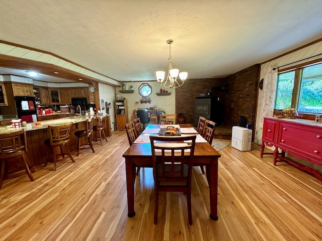 dining room with an inviting chandelier, brick wall, light hardwood / wood-style floors, and a textured ceiling