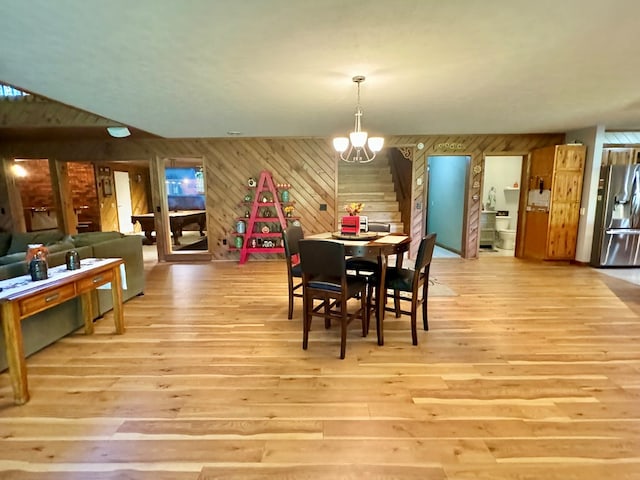 dining space with a notable chandelier, light wood-type flooring, and wood walls