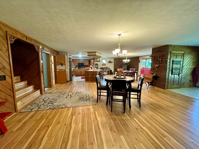 dining room with an inviting chandelier, wooden walls, a textured ceiling, and light wood-type flooring