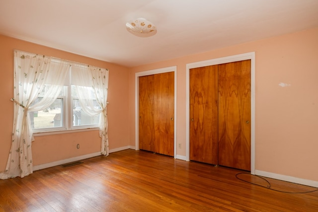 unfurnished bedroom featuring hardwood / wood-style flooring and multiple closets