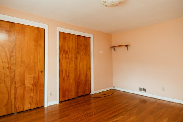 unfurnished bedroom with hardwood / wood-style flooring and multiple closets