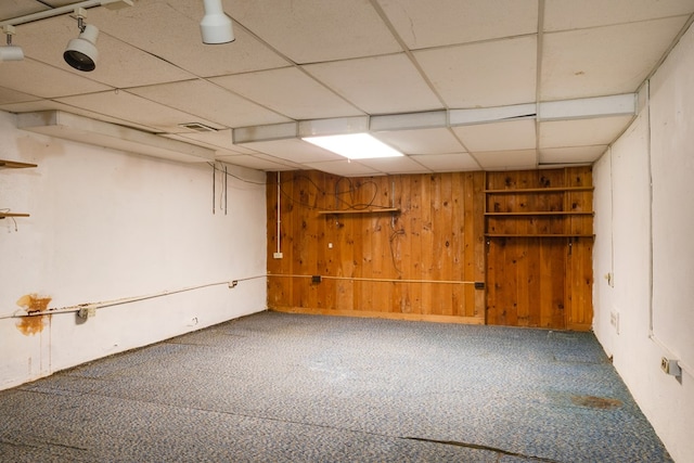 basement featuring a drop ceiling, wood walls, and carpet