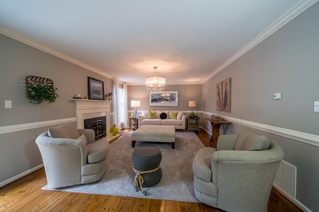 living room featuring a chandelier, ornamental molding, a tiled fireplace, and hardwood / wood-style floors