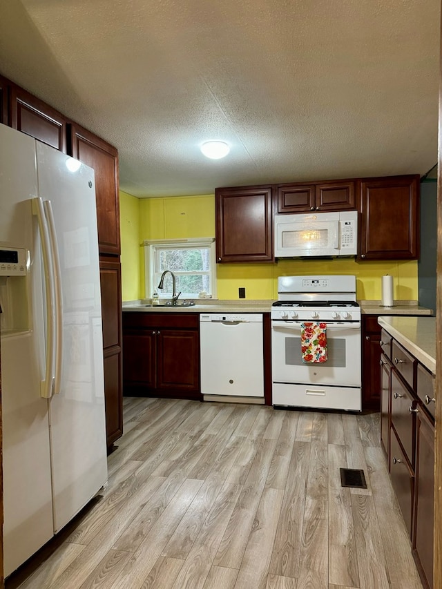 kitchen with white appliances, sink, light hardwood / wood-style flooring, and a textured ceiling