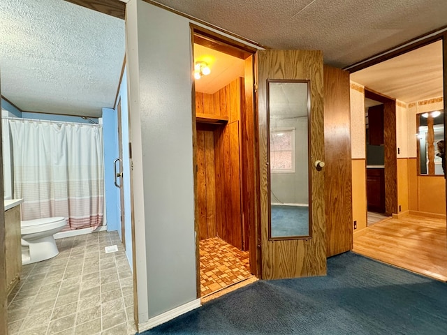 corridor featuring light colored carpet, a textured ceiling, and wood walls