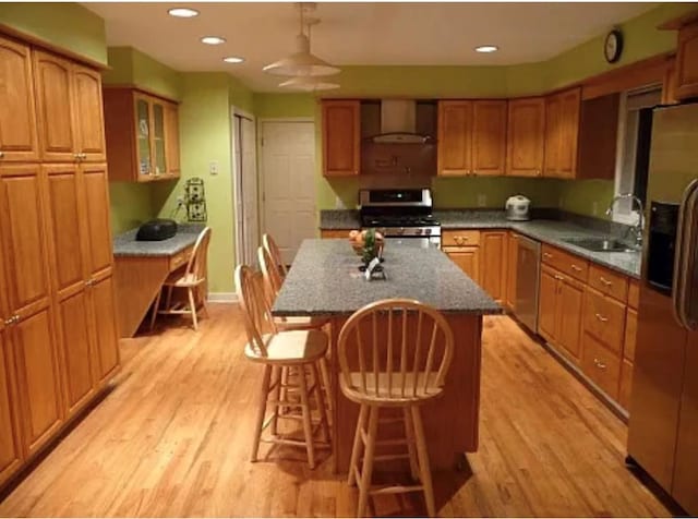 kitchen featuring appliances with stainless steel finishes, sink, a center island, light hardwood / wood-style floors, and wall chimney exhaust hood