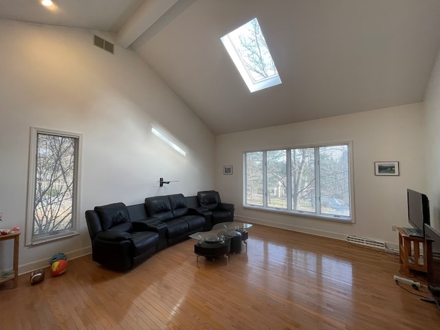 living room with beamed ceiling, high vaulted ceiling, a skylight, and light hardwood / wood-style floors