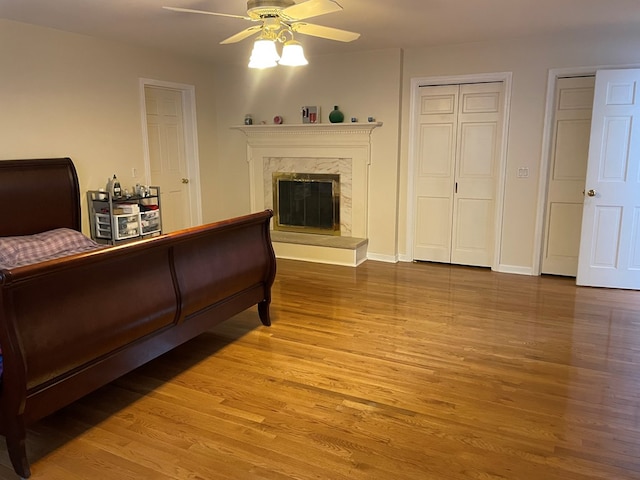 bedroom with ceiling fan, two closets, hardwood / wood-style floors, and a high end fireplace