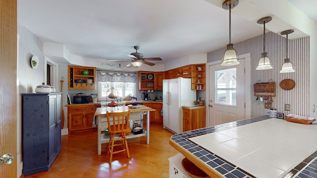 kitchen with tile countertops, light wood-type flooring, white refrigerator, pendant lighting, and ceiling fan