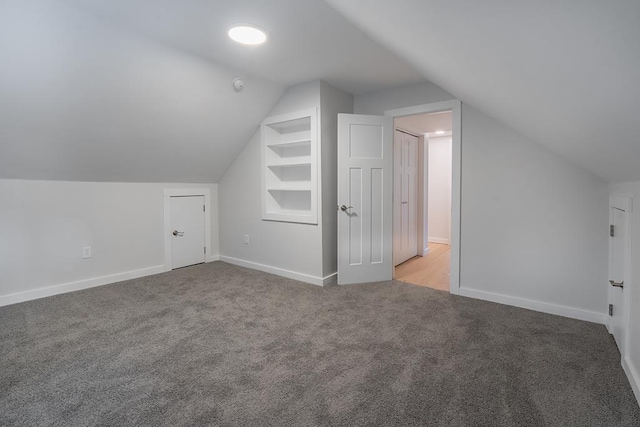 additional living space featuring built in shelves, lofted ceiling, and light carpet