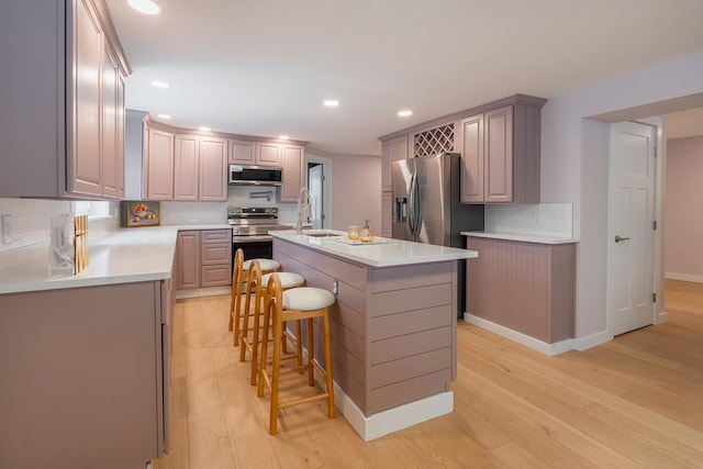 kitchen with a breakfast bar, sink, light wood-type flooring, appliances with stainless steel finishes, and a kitchen island