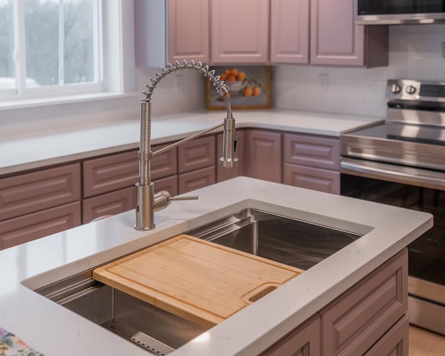 kitchen featuring stainless steel electric stove, sink, and decorative backsplash