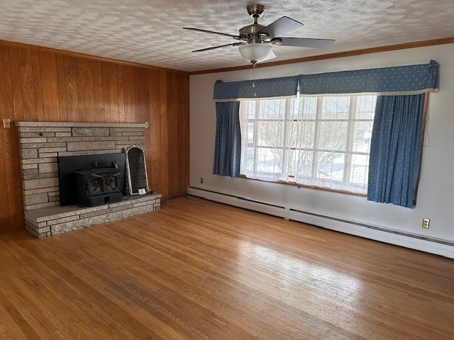 unfurnished living room with a healthy amount of sunlight, wood-type flooring, a baseboard heating unit, and ornamental molding