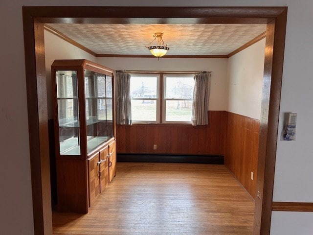 unfurnished dining area featuring a baseboard radiator, ornamental molding, light wood-type flooring, and wooden walls