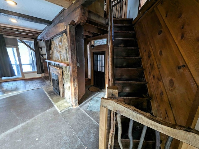 stairway featuring beamed ceiling and a stone fireplace