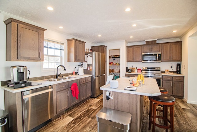 kitchen with sink, appliances with stainless steel finishes, ornamental molding, a kitchen island, and dark hardwood / wood-style flooring