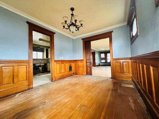 unfurnished dining area with wood-type flooring, ornamental molding, and a chandelier