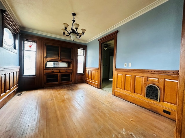 unfurnished living room featuring an inviting chandelier, crown molding, and light hardwood / wood-style flooring