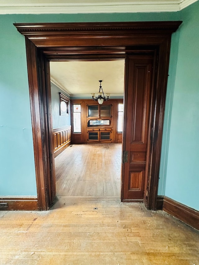 hall featuring crown molding, light hardwood / wood-style flooring, and a notable chandelier