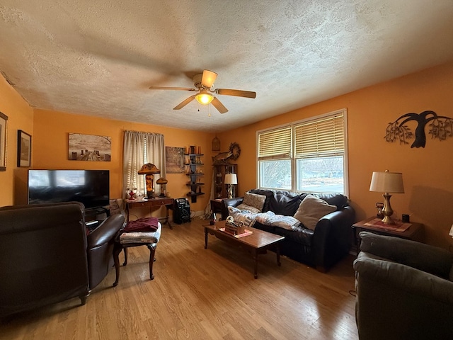 living room with ceiling fan, a textured ceiling, and light wood-type flooring