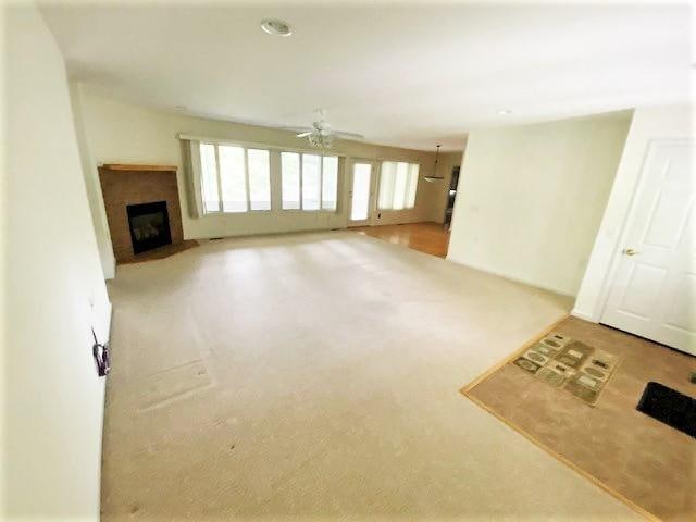 unfurnished living room with light colored carpet and ceiling fan