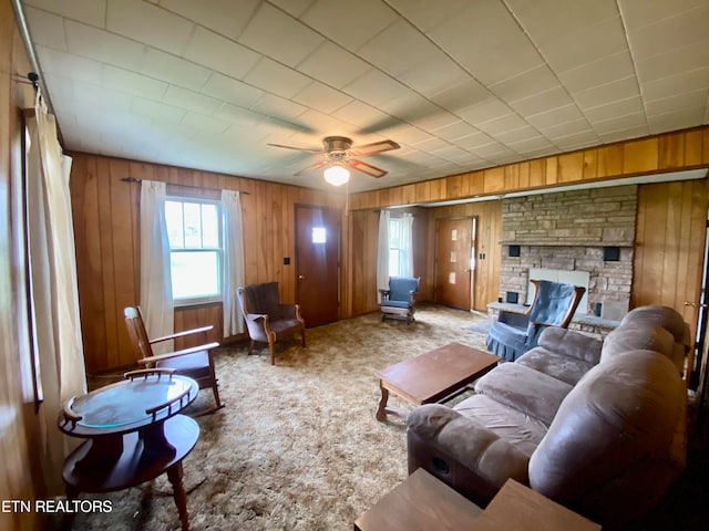 living room with light colored carpet, wood walls, a stone fireplace, and ceiling fan