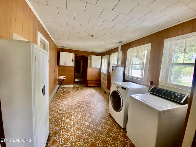 clothes washing area featuring dark tile floors, water heater, wooden walls, and washer and clothes dryer