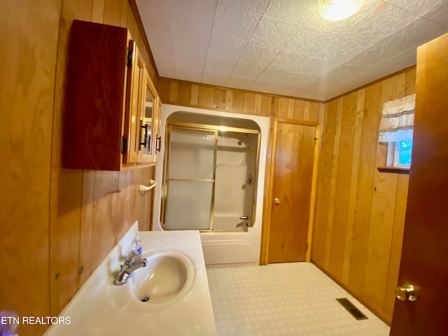 bathroom with wood walls, shower / bathing tub combination, and sink