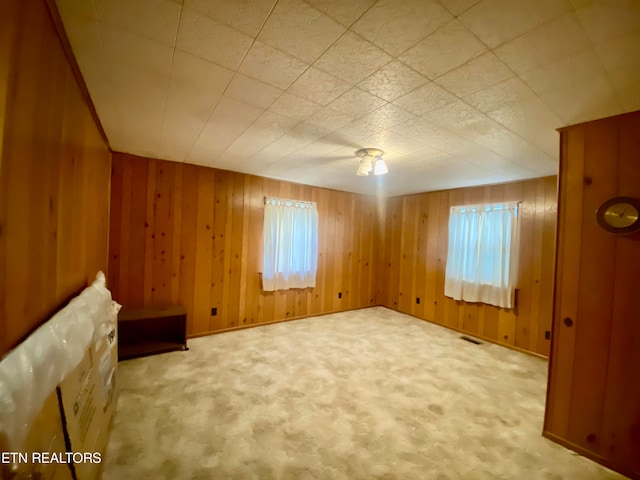 unfurnished room with a wealth of natural light, light carpet, and wood walls