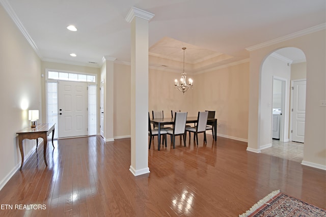 foyer with crown molding, hardwood / wood-style floors, baseboards, arched walkways, and washer / dryer