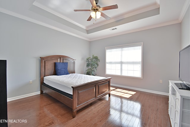 bedroom with baseboards, visible vents, wood finished floors, and a raised ceiling