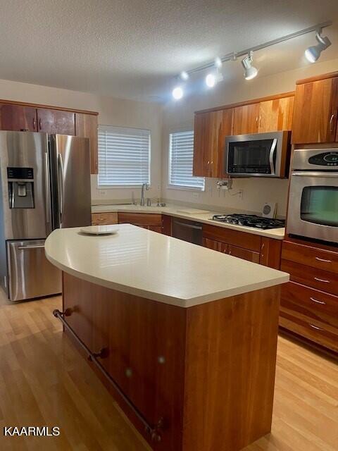 kitchen with stainless steel appliances, track lighting, a center island, light wood-type flooring, and a textured ceiling