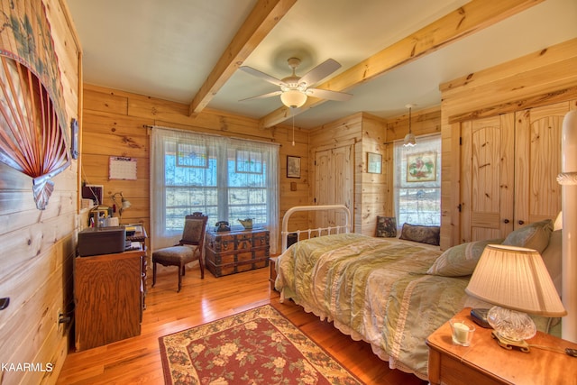 bedroom with ceiling fan, beam ceiling, light wood-type flooring, and wooden walls