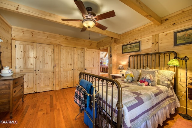 bedroom featuring beamed ceiling, hardwood / wood-style floors, ceiling fan, and wooden walls