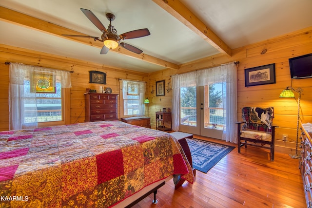 bedroom featuring french doors, wooden walls, ceiling fan, access to exterior, and beamed ceiling