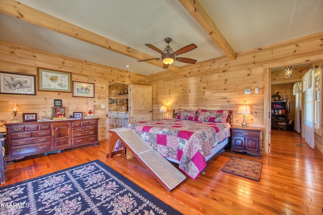 bedroom featuring beam ceiling, ceiling fan, light hardwood / wood-style flooring, and wood walls