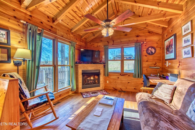 living room with wood walls, ceiling fan, light wood-type flooring, beam ceiling, and wood ceiling