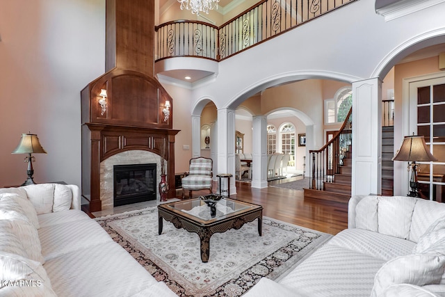 living room featuring ornate columns, a notable chandelier, a towering ceiling, and wood-type flooring