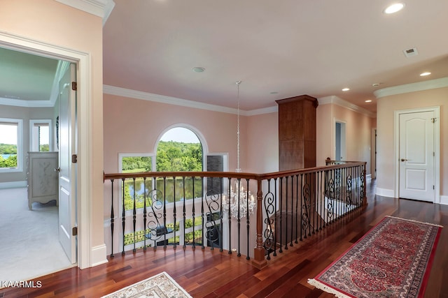 hall featuring crown molding, dark carpet, an inviting chandelier, and a wealth of natural light