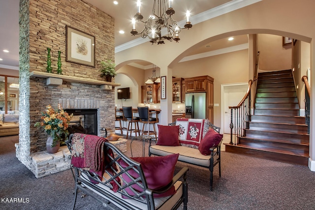 living room featuring a chandelier, a towering ceiling, dark colored carpet, a fireplace, and ornamental molding