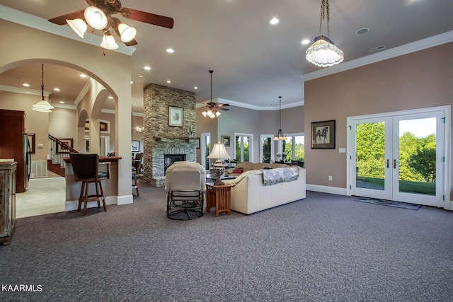 living room with carpet flooring, ceiling fan, french doors, ornamental molding, and a stone fireplace