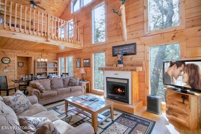 living room featuring light wood-type flooring, ceiling fan with notable chandelier, wood walls, and high vaulted ceiling