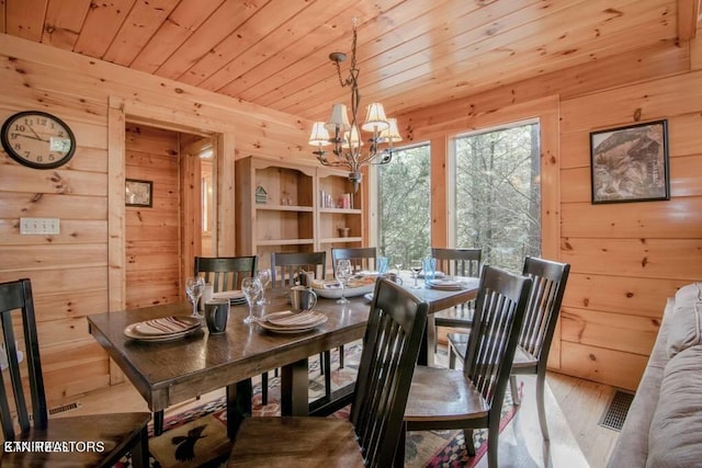 dining room featuring an inviting chandelier, wooden walls, light wood-type flooring, and wood ceiling